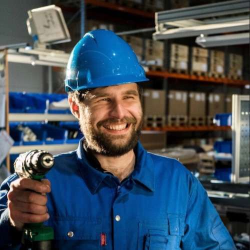 Headshot picture of Tomasz in blue overalls and a blue hardhat while holding a drill for About.